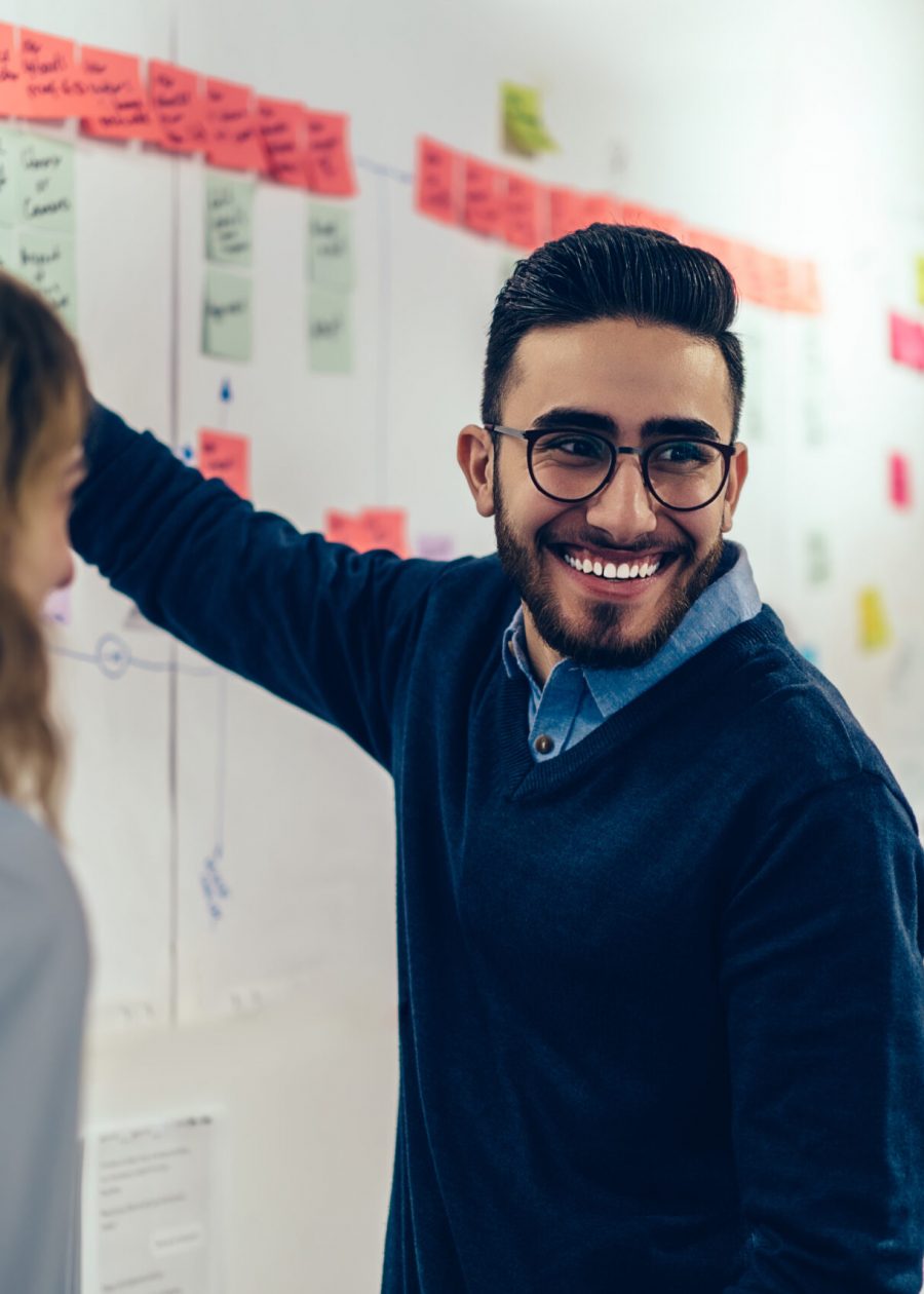 Positive young man laughing while collaborating with colleagues on creating presentation using colorful stickers for productive work in office.Male and female students having fun during workshop